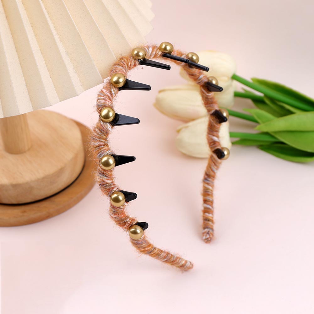 Decorative SheFav headband with gold beads and black spikes on a light pink background